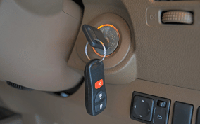 Car key inserted into ignition with key fob hanging.